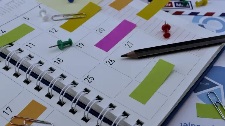 Notizbuch mit Stift, Haftnotizen und Büroklammern auf einer Tischoberfläche.